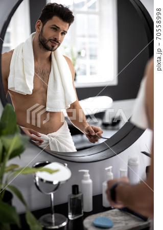 Waist up shot of man looking to himself through the mirror Waist up shot of man looking to himself through the mirror 70558998
