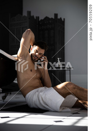 Handsome man wrapped in towel talking on mobile phone and sitting on floor 70559209