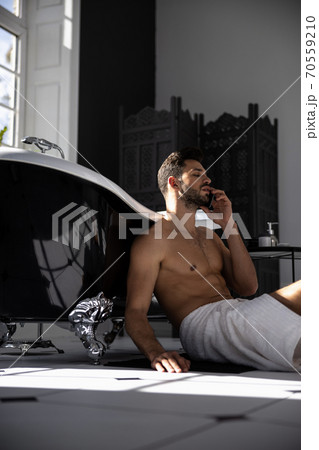Handsome man wrapped in towel talking on mobile phone and sitting on floor 70559210