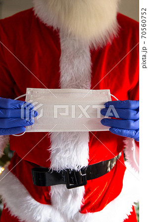 Man wearing santa claus costume holding safety mask and wearing protective gloves for Coronavirus, Covid-19 and Christmas concept Man wearing santa claus costume holding safety mask and wearing protective gloves for Coronavirus, Covid-19 and Christmas concept 70560752