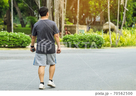 Back view portrait of a Asian man in fitness wear walking and jogging for good health in public park. Jogger in nature. Man enjoying Peaceful nature. Healthcare concept. 70562500