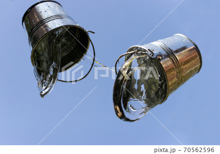 A falling buckets splashes water, on a background of blue sky. A falling buckets splashes water, on a background of blue sky. 70562596