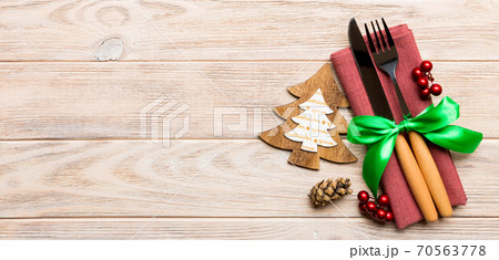 Top view of fork and knife tied up with ribbon on napkin on wooden background. Christmas decorations and New Year tree. Banner Happy holiday concept with empty space for your design Top view of fork and knife tied up with ribbon on napkin on wooden background. Christmas decorations and New Year tree. Banner Happy holiday concept with empty space for your design 70563778