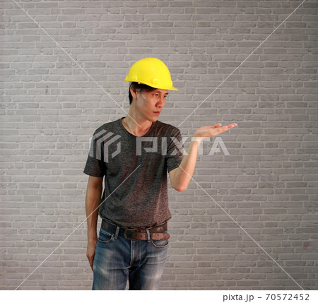 technician man ware yellow helmet with dark grey T-shirt and denim jeans standing palms facing up 70572452