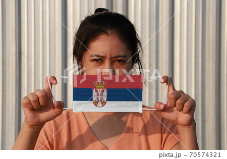 A woman with Serbia flag on hygienic mask in her hand and lifted up the front face 70574321