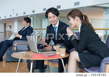 ビジネス　ロビーで打ち合わせをする若い笑顔の男女と英字新聞を読むミドルエイジの男性 70576785