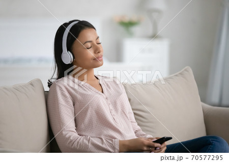 Young biracial woman in headphones listen to music on cell Young biracial woman in headphones listen to music on cell 70577295