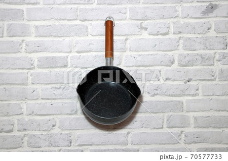 Boil pot with long wooden handle hanging on the brick pattern wall. 70577733
