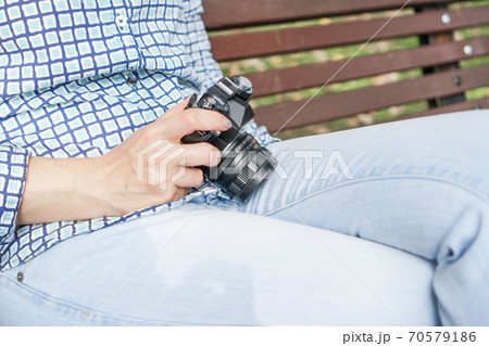 Antique camera in the hands of a girl in blue jeans and a blue shirt. On a park bench. Preparing for a photo shoot Antique camera in the hands of a girl in blue jeans and a blue shirt. On a park bench. Preparing for a photo shoot 70579186