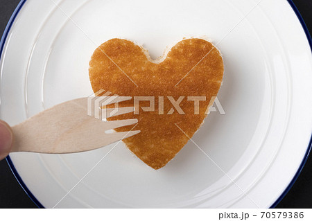 Cupcake in the shape of a heart of golden color on a white plate with a blue border. Wooden eco fork pierces it. The concept of useful bio dessert 70579386
