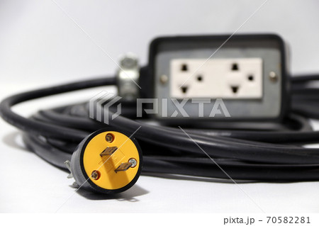 Yellow plug and out focus outlet with black cable on the white background.  70582281