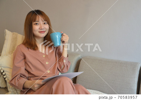 マグカップを片手に書類を持つ若い女性 70583957