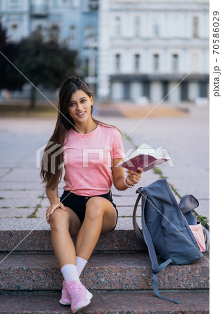 Cheerful young woman taking notes while sitting on steps otdoors 70586029