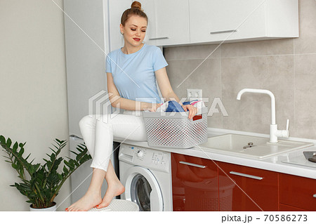 Woman uses a washing machine in the kitchen Woman uses a washing machine in the kitchen 70586273