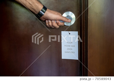 Close up of a hand opening disinfected hotel room. A sign hanging on the handle saying the room has been sanitized. New Normal, travel under Covid-19 pandemic, vacation and holiday concept 70589043