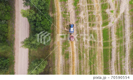 Aerial view of tractor with baler rolling bales of straw on harvested field. Top view. Aerial view of tractor with baler rolling bales of straw on harvested field. Top view. 70590554
