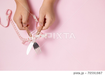 Fat boy hand holding knife and fork wrapped in measuring tape Fat boy hand holding knife and fork wrapped in measuring tape 70591987