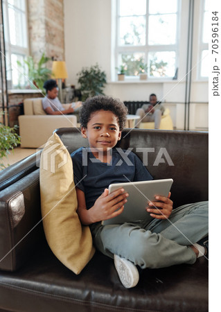 Adorable little boy in casualwear sitting on couch and watching online video Adorable little boy in casualwear sitting on couch and watching online video 70596184