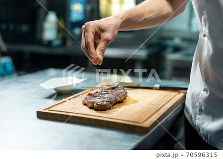 Hand of chef sprinkling spices on roasted beef steak during preparation 70596315