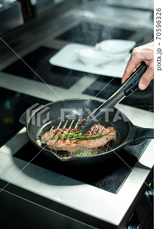 Hand of chef frying piece of beef and adding fresh aromatic herbs to the meat Hand of chef frying piece of beef and adding fresh aromatic herbs to the meat 70596326