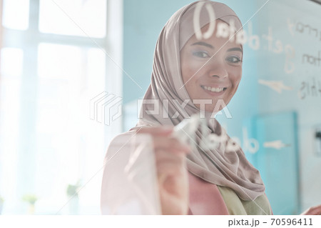 Young smiling Muslim female broker in hijab making notes with highlighter 70596411