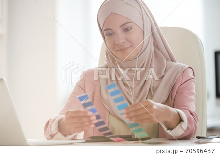 Young pretty Muslim female designer comparing two color palettes at work 70596437