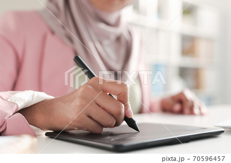 Hand of young contemporary female designer in hijab holding stylus over tablet Hand of young contemporary female designer in hijab holding stylus over tablet 70596457
