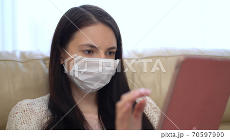 Woman in a Medical Mask Uses a Tablet at Home During Quarantine. Works Alone From Home Remotely. Quarantine Covid-19 Corona Virus. Social Distancing Concept. Woman in a Medical Mask Uses a Tablet at Home During Quarantine. Works Alone From Home Remotely. Quarantine Covid-19 Corona Virus. Social Distancing Concept. 70597990