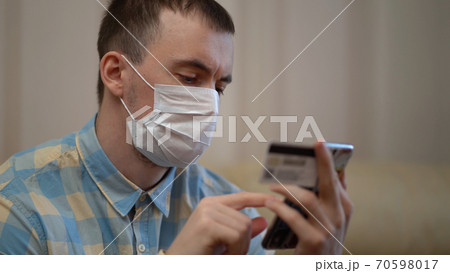 Quarantine Covid-19 Coronavirus. Man with Mask Shopping Online with Credit Card Using Smart Phone at Home. Food Delivery , Paying Order. Social Distancing. 70598017