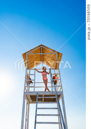 teenage girl stands on lifeguard tower on beach  70598509