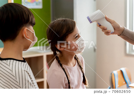Group of Caucasian students in school building checked and scanned for temperature check. Elementary pupils are wearing a face mask and line up before entering into classroom. Group of Caucasian students in school building checked and scanned for temperature check. Elementary pupils are wearing a face mask and line up before entering into classroom. 70602650