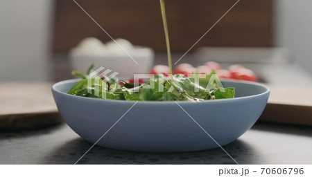 closeup add oil to mixed salad leaves in a blue bowl on concrete countertop 70606796