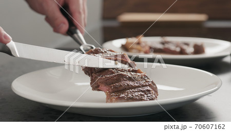 Man put sliced ribeye steak on a white plate on concrete countertop Man put sliced ribeye steak on a white plate on concrete countertop 70607162