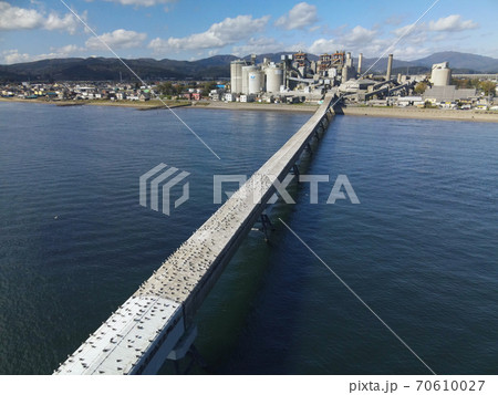秋の北海道北斗市でセメント工場に荷卸しをする貨物船とベルトコンベアーの風景を空撮 70610027