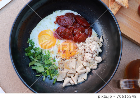 pan fried egg with toppings, Chinese sausage and pork sausage in the black pan. 70615548