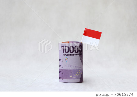 Banknote money ten thousand Indonesia Rupiah and mini Indonesia flag on the white floor. Banknote money ten thousand Indonesia Rupiah and mini Indonesia flag on the white floor. 70615574