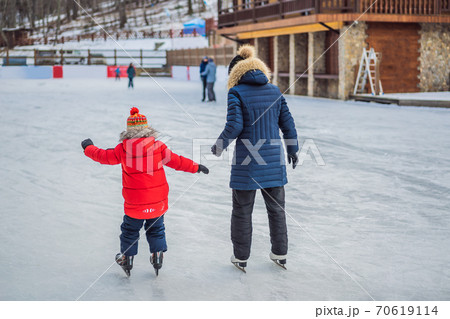 young mother teaching her little son ice skating at outdoor skating rink. Family enjoy winter on ice-rink outdoors 70619114