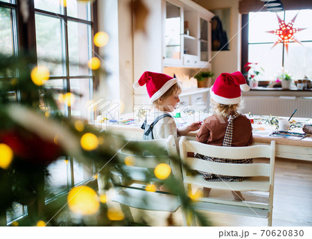 Rear view of small girl and boy indoors at home at Christmas, painting pictures. 70620830