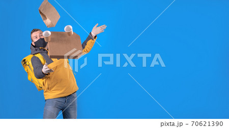 Food delivery man in yellow uniform, wearing mask and gloves, slipped, lost his balance, and hurled box of food from restaurant. Clumsy food vendor tore up customer's order. Poor product delivery Food delivery man in yellow uniform, wearing mask and gloves, slipped, lost his balance, and hurled box of food from restaurant. Clumsy food vendor tore up customer's order. Poor product delivery 70621390