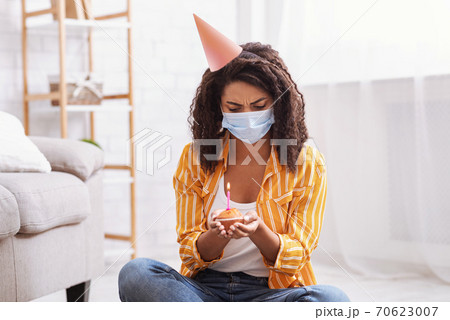 Unhappy black woman in party hat celebrating birthday alone 70623007