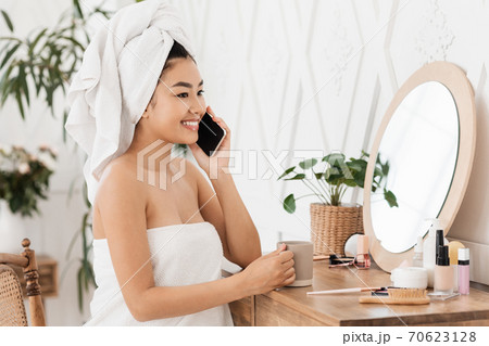 Happy asian woman talking on phone, sitting next to mirror 70623128