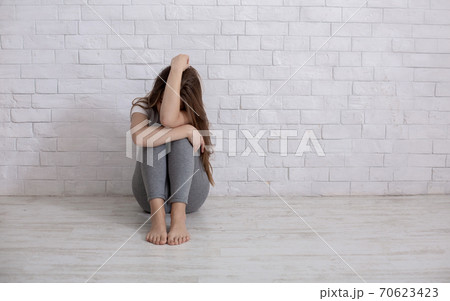 Desperate young lady crying from hopelessness on floor near white wall, blank space Desperate young lady crying from hopelessness on floor near white wall, blank space 70623423