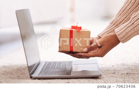 Woman showing gift box to laptop screen 70623436