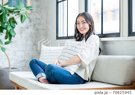 クッションを抱いてリビングでくつろぐ若い女性　 70625945
