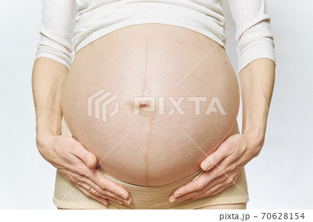 A faceless pregnant woman holds her belly with her hands. close-up 70628154