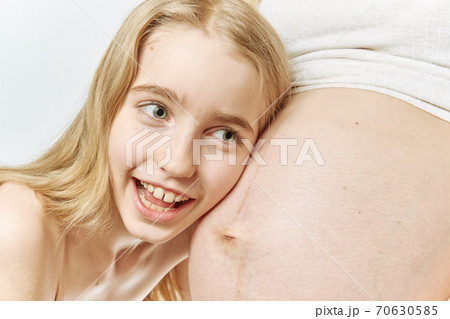 A blonde Caucasian girl hugs and listens to the belly of her pregnant A blonde Caucasian girl hugs and listens to the belly of her pregnant 70630585