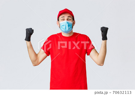 Covid-19, self-quarantine, online shopping and shipping concept. Excited delivery man feel rejoice and happiness, fist pump in celebration, success, achieve goal, wear medical mask and uniform cap 70632113