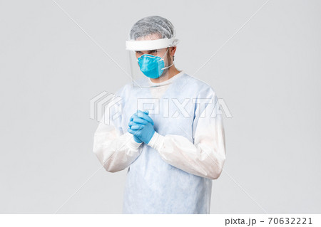 Covid-19, pandemic, healthcare workers fighting virus outbreak. Thoughtful and caring doctor in personal protective equipment, medical mask and gloves, praying god, safe patient lives coronavirus 70632221