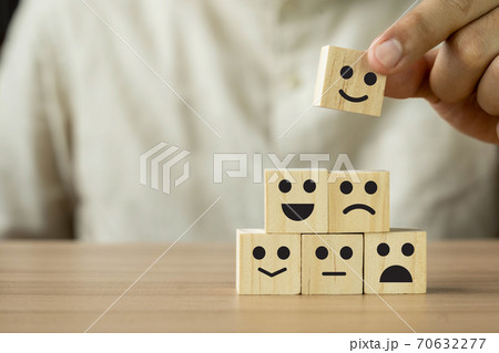 Close up Hand holding of Happy icon on cube blocks about service rating feedback of survey from customer. Business annual satisfaction survey concept. Many sad or happily on wooden table.copy space 70632277