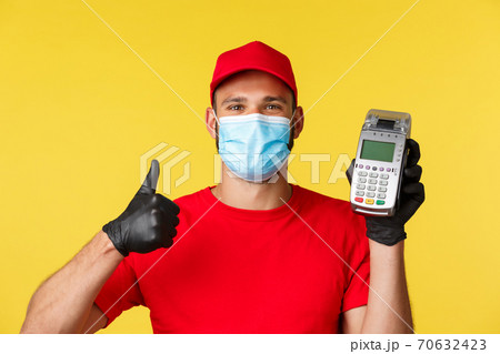 Covid-19, delivery orders, shopping, contactless payment and social distancing concept. Satisfied handsome courier in red uniform, advice use POS terminal for safety during coronavirus pandemic 70632423
